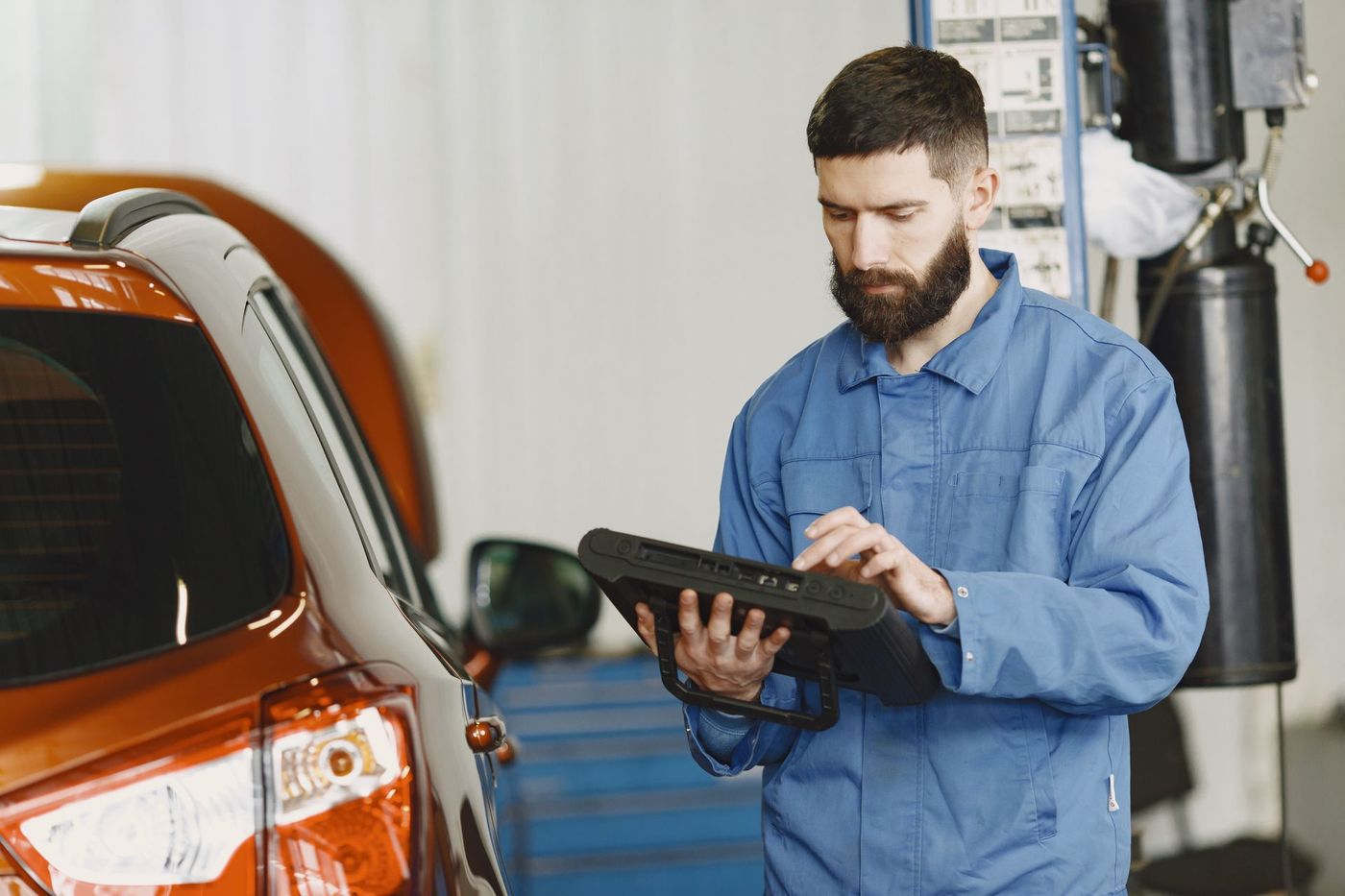 Technician reading a handheld automotive diagnostic tool beside a car