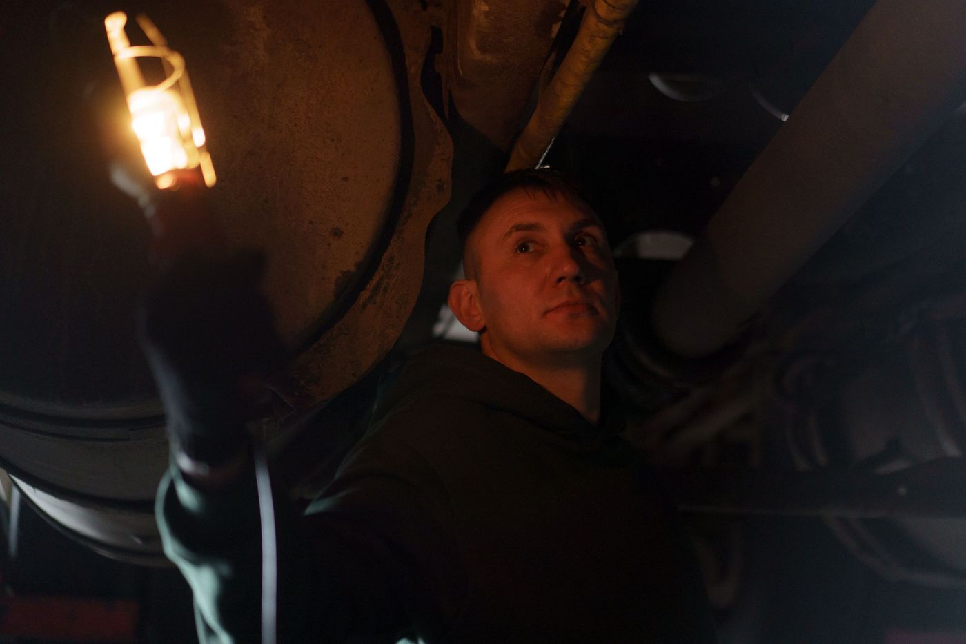 Mechanic holding a work lamp while working on a vehicle after dark